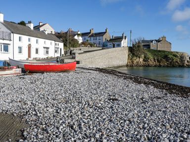 A pebble beach with boats near white houses and a stone wall by the water at 22 Gwel Yr Wyddfa in Menai Bridge