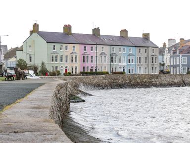 Row of colorfully painted houses along a stone seawall beside a body of water at 22 Gwel Yr Wyddfa in Menai Bridge