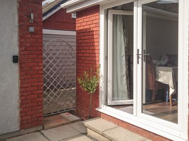 A patio area with glass doors open to a dining room and a small potted plant near a red brick wall at 22 Gwel Yr Wyddfa Menai Bridge