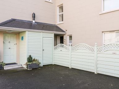 An exterior area with a light green door and storage shed next to a cream building and three light green wooden fences