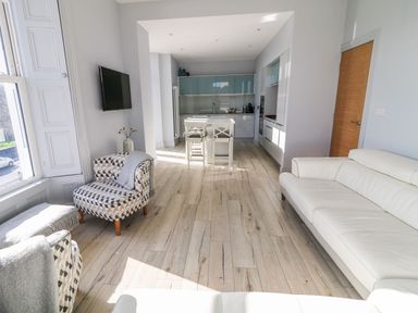 A living room with patterned armchairs white sofa wall-mounted tv and kitchen area at Sea Breeze in Ballycastle