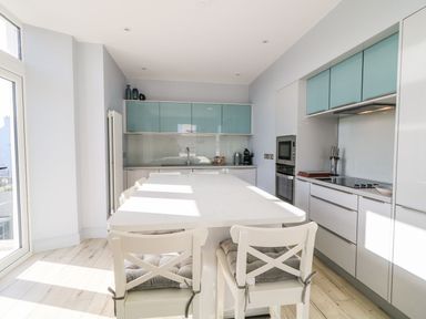 A kitchen with white island and chairs and teal cabinets at Sea Breeze in Ballycastle