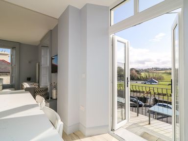 A dining area with white chairs and a marble table next to an open door leading to a balcony with a view of a green field at Sea Breeze in Ballycastle