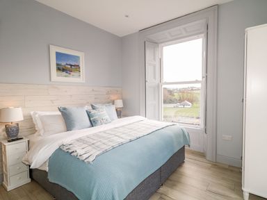 A bedroom with a bed pillows lamps a window and a wardrobe at Sea Breeze in Ballycastle