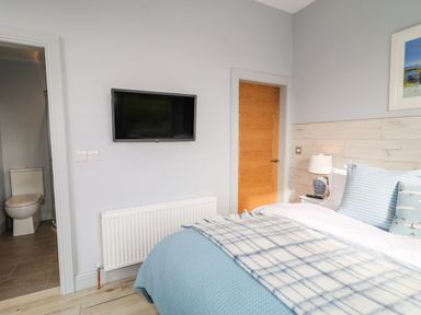 A bedroom with a bed with blue and white bedding a wall mounted television a wooden door and an open bathroom door at Sea Breeze in Ballycastle