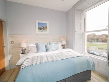 A bedroom with a bed with blue bedding a window bedside tables and lamps at Sea Breeze in Ballycastle