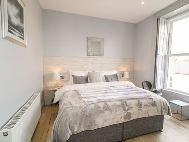 A bedroom with a large bed bedside tables lamps a window and a radiator at Sea Breeze in Ballycastle