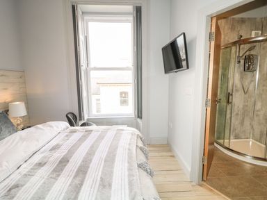 A bedroom with a bed a window a wall-mounted television and an open door leading to a shower at Sea Breeze in Ballycastle