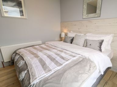 A bedroom with a bed pillows a blanket a lamp and a mirror at Sea Breeze in Ballycastle
