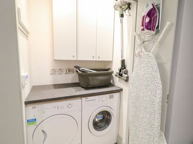 A laundry room with a washing machine dryer countertop storage baskets ironing board iron and cordless vacuum