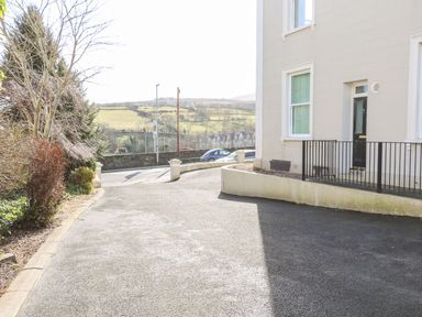 A paved driveway next to a building with a door and windows with hills and trees in the background at Sea Breeze in Ballycastle