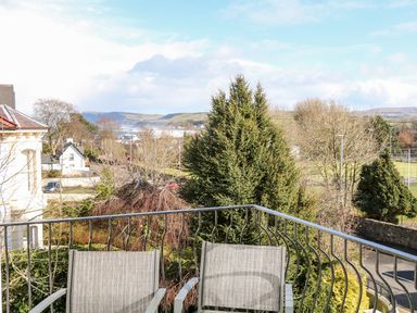 A balcony with two chairs overlooking trees houses and hills at Sea Breeze in Ballycastle