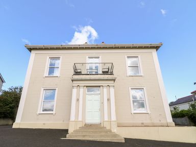 A two-story beige building with six windows and a white front door with columns and a small balcony above at Beachcomber in Ballycastle