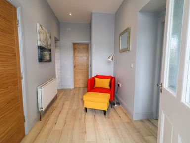 A hallway with a red chair and yellow ottoman next to a floor lamp and mirror at Beachcomber Ballycastle