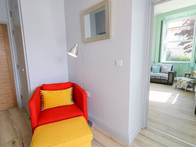 A red armchair with a yellow cushion and matching ottoman next to a silver floor lamp in a room with light-colored wooden flooring at Beachcomber in Ballycastle