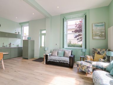 A living room with sofas a window a kitchen area and wooden flooring at Beachcomber in Ballycastle