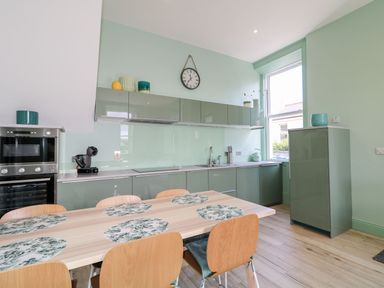 A kitchen with a dining table and wooden chairs next to green cabinets and a window at Beachcomber in Ballycastle
