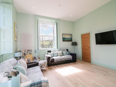 A sitting room with two sofas an armchair a floor lamp a wall-mounted tv and a window with a countryside view at Beachcomber in Ballycastle