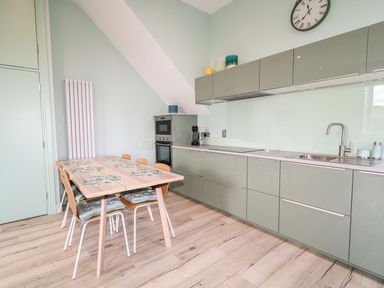 A kitchen with a dining table and chairs beside cabinets with a sink and oven at Beachcomber in Ballycastle