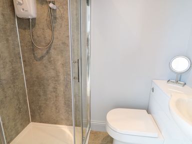 A bathroom with a shower cubicle and a toilet next to a vanity unit with a mirror at Beachcomber in Ballycastle