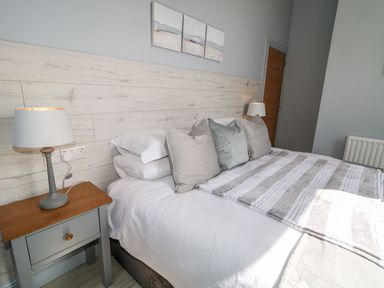 A bedroom with a bed with pillows and a striped blanket and two bedside tables with lamps at Beachcomber in Ballycastle
