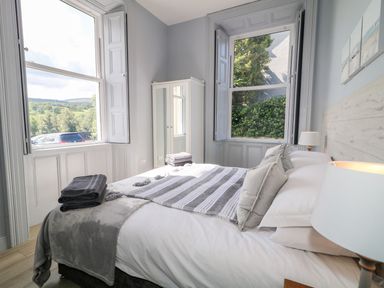 A bedroom with a bed pillows and towels near two windows with greenery outside at Beachcomber in Ballycastle