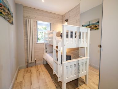 A small bedroom with white bunk beds wooden flooring a window and paintings on the wall at Beachcomber in Ballycastle
