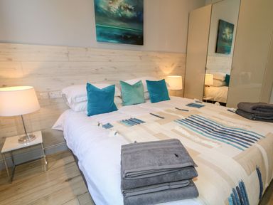 A bedroom with a bed with white sheets and blue pillows next to bedside tables with lamps and a wardrobe with mirrored doors at Beachcomber in Ballycastle