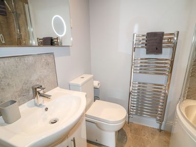 A bathroom with a white sink a toilet a towel rack with a gray towel and a mirror at Beachcomber in Ballycastle