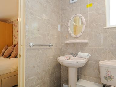 A bathroom with a floral decorated sink, mirror, and toilet adjacent to a bedroom at Dart Lodge in Callington