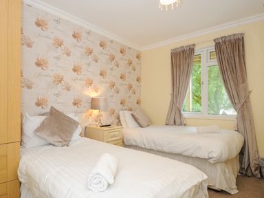 A bedroom with two single beds a nightstand lamp window with curtains and floral wallpaper at Dart Lodge in Callington