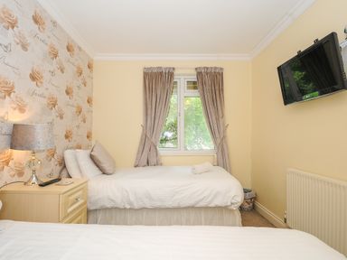 A bedroom with two single beds nightstand with lamp and TV mounted on wall at Dart Lodge in Callington