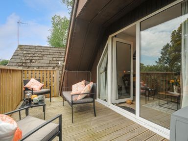An outdoor wooden deck with chairs and cushions next to a glass sliding door at Dart Lodge in Callington