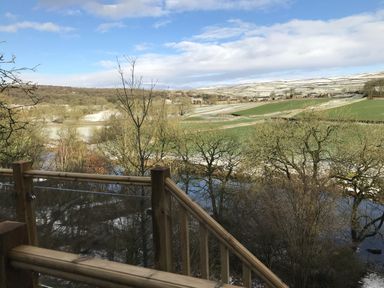 A view of a river and fields from a wooden railing at The Sett on the Wharfe Skipton