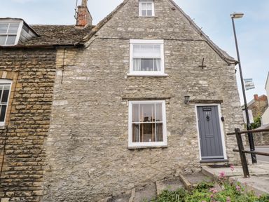 Stone exterior of a house with two windows and a gray door at Corner Cottage in Malmesbury