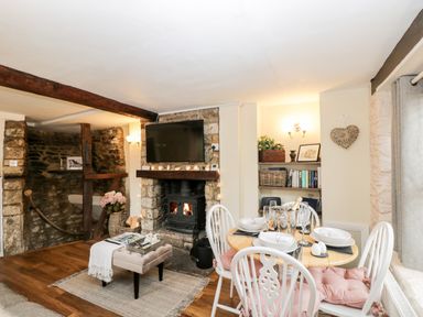 A dining area with a round table set for four next to a fireplace with a TV above at Corner Cottage in Malmesbury