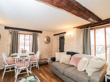 A living room with a gray sofa with pillows and a dining table with four white chairs at Corner Cottage in Malmesbury