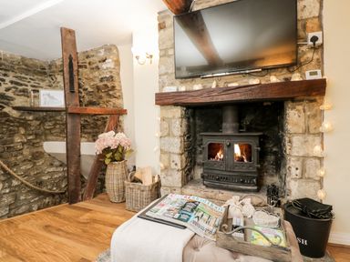 A living room corner with a stone fireplace wood stove and a mounted television at Corner Cottage in Malmesbury
