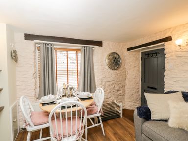 A dining area with a round table set for four and a grey sofa near a dark door at Corner Cottage in Malmesbury