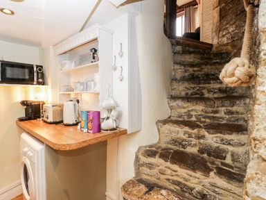 A kitchen counter with appliances and a stone staircase with a rope handrail at Corner Cottage in Malmesbury