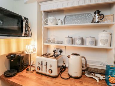 A kitchen countertop with a toaster kettle coffee machine microwave jars and a small lamp at Corner Cottage Malmesbury