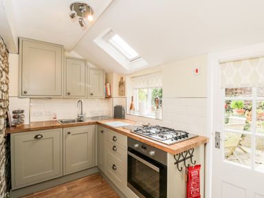 A kitchen with wooden countertops gas stove oven sink cabinets and a door leading outside at Corner Cottage in Malmesbury