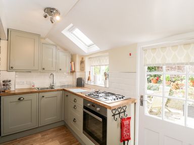 A kitchen with wooden countertops cabinets a gas stove oven a sink and a door leading to an outdoor seating area at Corner Cottage in Malmesbury