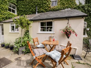 A small outdoor patio with a wooden table and four chairs with cushions at Corner Cottage in Malmesbury