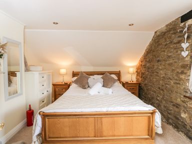 A bedroom with a wooden bed two bedside tables with lamps a stone wall and a dresser at Corner Cottage in Malmesbury