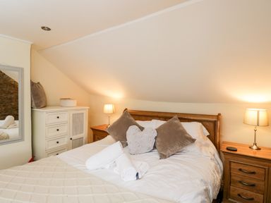 A bedroom with a wooden bed with pillows and rolled towels beside two wooden bedside tables with lamps at Corner Cottage in Malmesbury