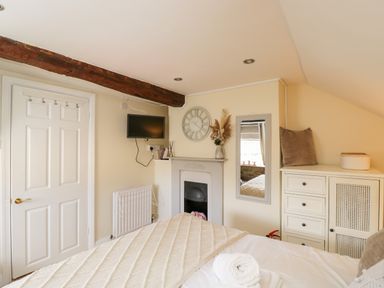 A bedroom with a bed a wall-mounted tv a fireplace a wall clock a mirror and a cabinet at Corner Cottage in Malmesbury