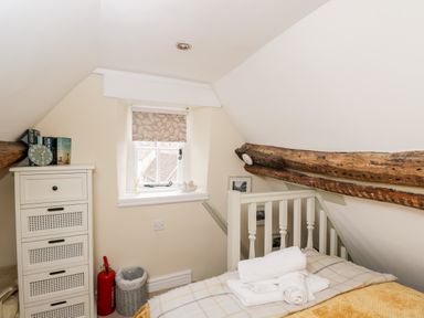 A small bedroom with a bed towel set chest of drawers window and wooden ceiling beam at Corner Cottage in Malmesbury