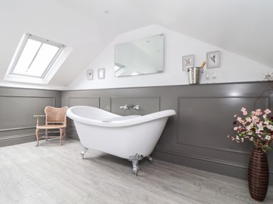 A bathroom with a white clawfoot bathtub a wooden chair a vase with flowers and a skylight window at Rock Pool House in Porthleven