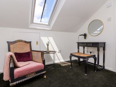 A room with a chair a small round table a vanity table with a mirror and a skylight window at Rock Pool House in Porthleven